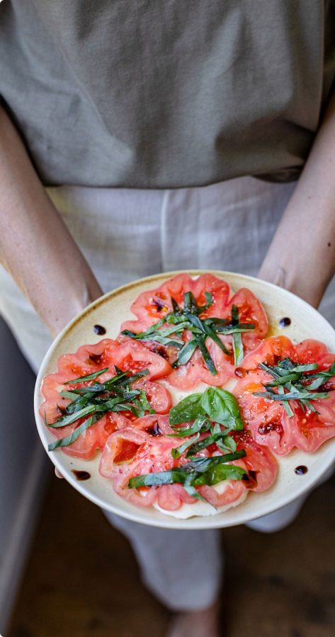 Persona sosteniendo plato de tomate con un carpaccio de rodajas tomate Monterosa.