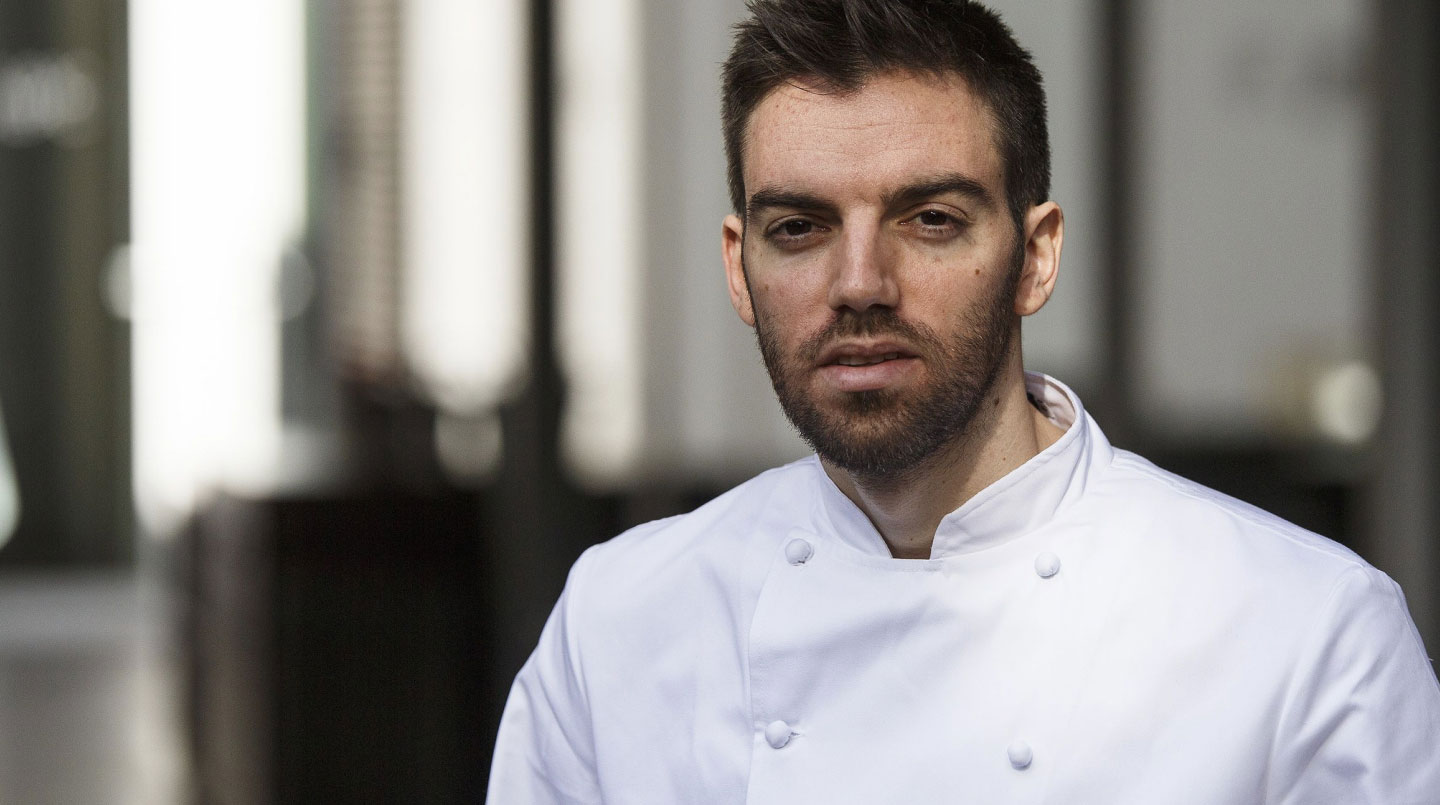 David Andres. Colaboraciones con tomate Monterosa. En la imagen una foto de el con chaqueta blanca de cocinero.