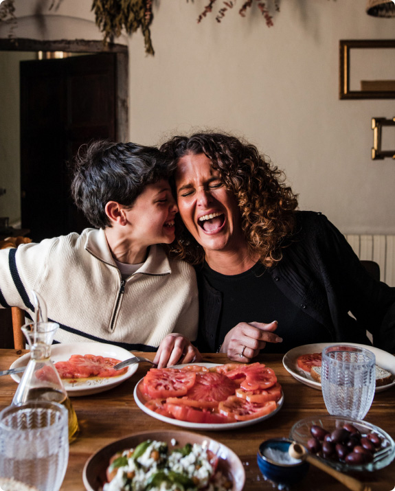 En la imagen aparece un niño y su madre mientras compartiendo un delicioso tomate Monterosa partido. Una imagen familiar. La madre y el niño ríen a carcajadas transmitiendo felicidad