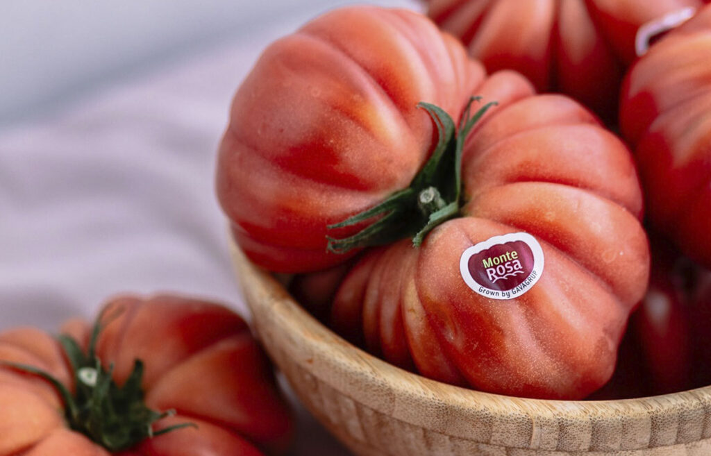 Imagen de tomates Monterosa en un cesto, alguno fuera de ella. Es una imagen con aire rústico que enfoca con detalle el tomate.
