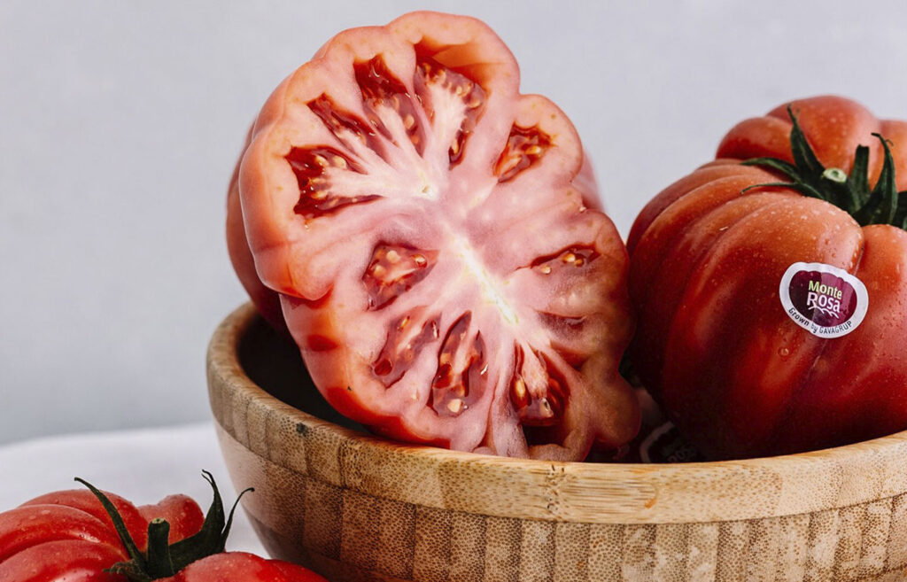 Imagen de tomates Monterosa en un cesto, alguno fuera de ella. Uno de ellos esta partido para poder ver en detalle como son por dentro. Es una imagen para enlazar a donde explicamos lo bien que son para la nutricion y como es su sabor.