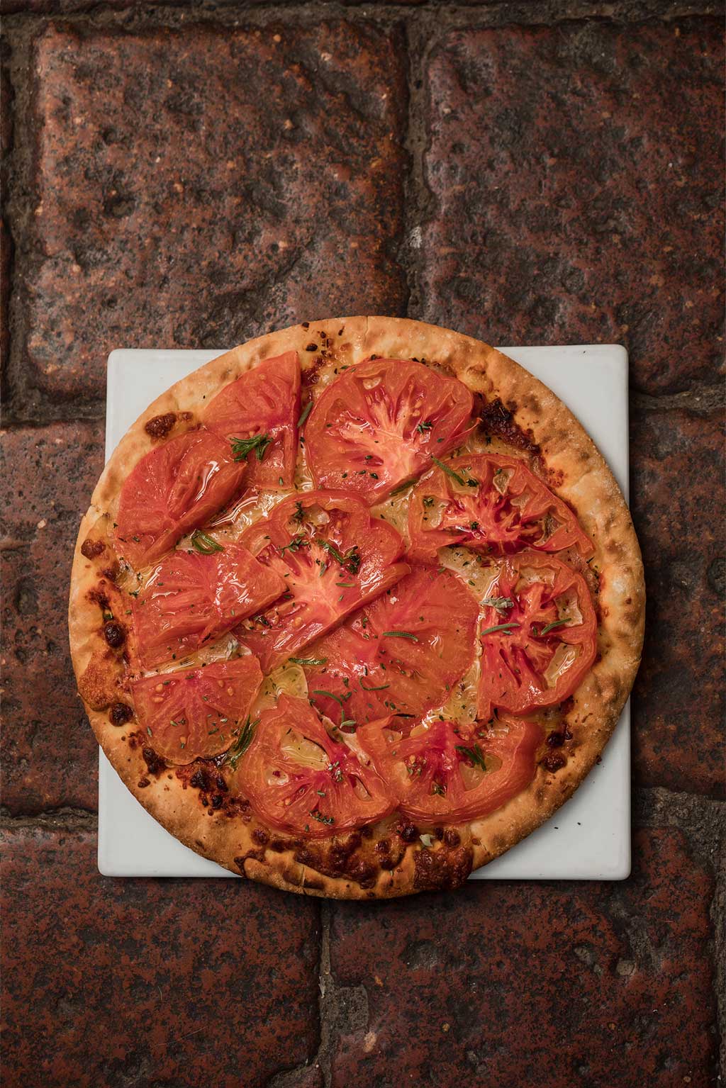 Receta de pizza con Tomate Monterosa. Vista desde arriba sobre un plato cuadrado en una mesa de piedra marrón oscura.